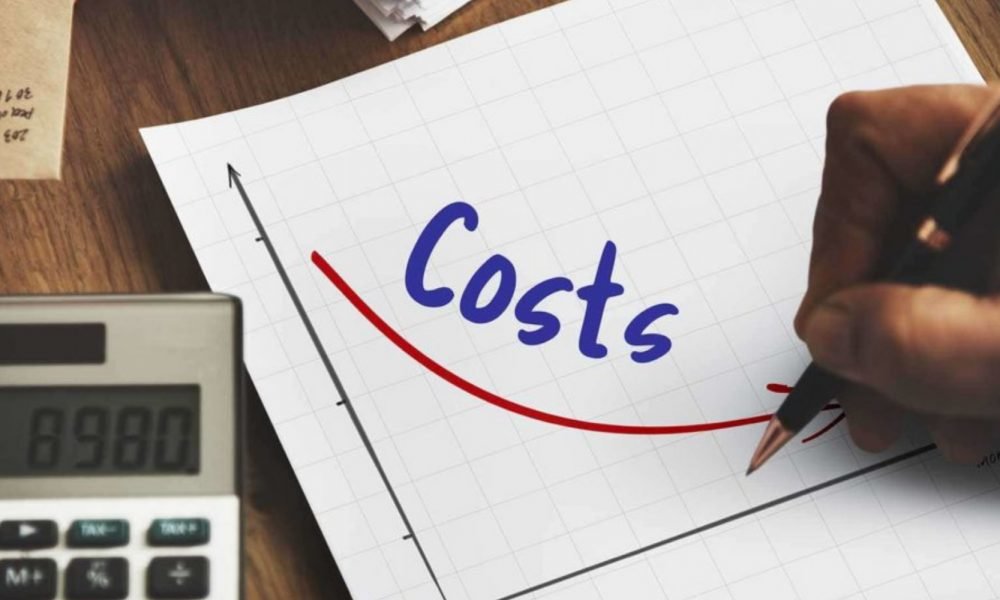  A person is writing the word 'costs' on a notepad with a downward arrow next to it, a calculator is sitting next to the notepad. The image represents the search query 'Tips for minimizing shopping expenses'.